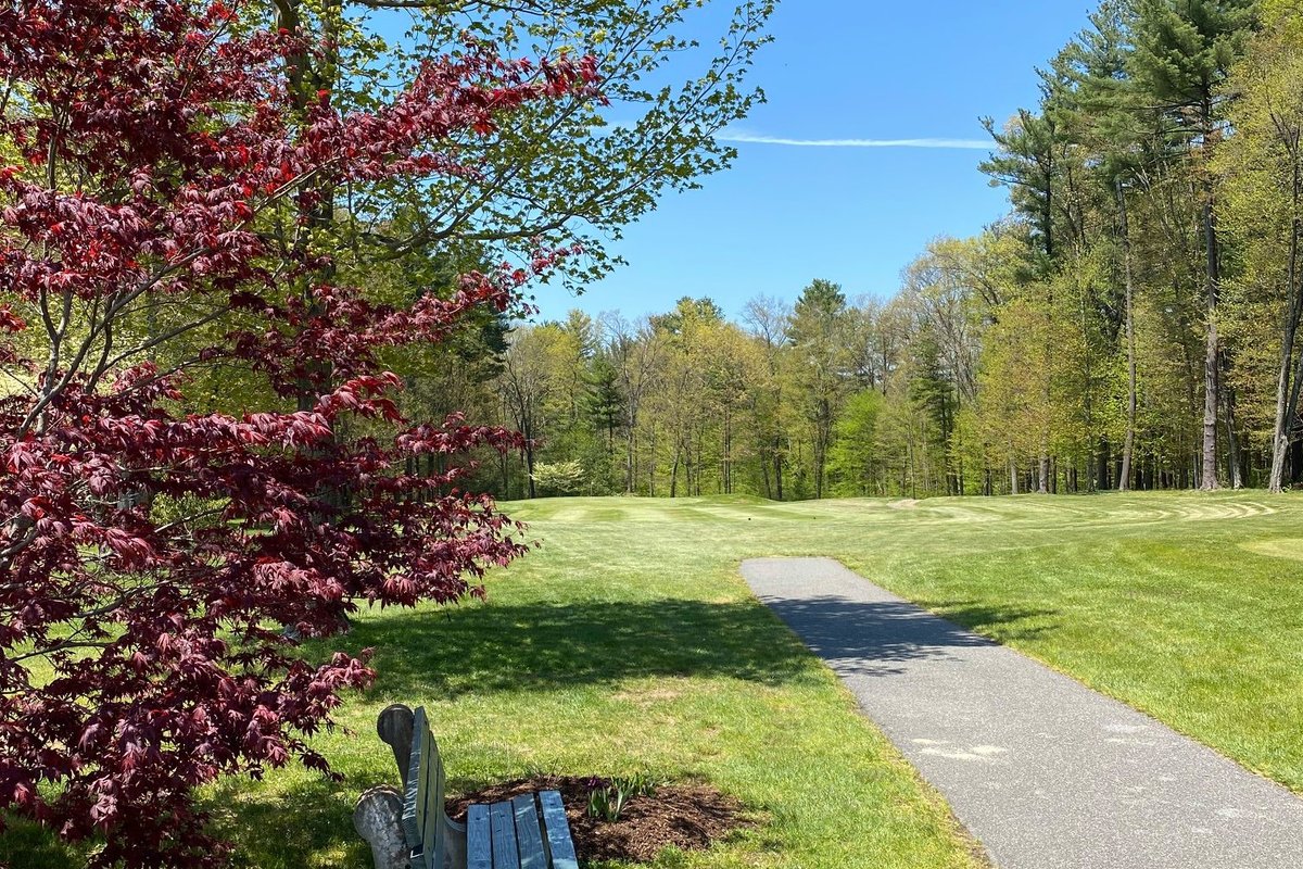 Golf cart path winding through green fairway at Country Club of Wilbraham, bordered by trees and red-leafed foliage under blue sky