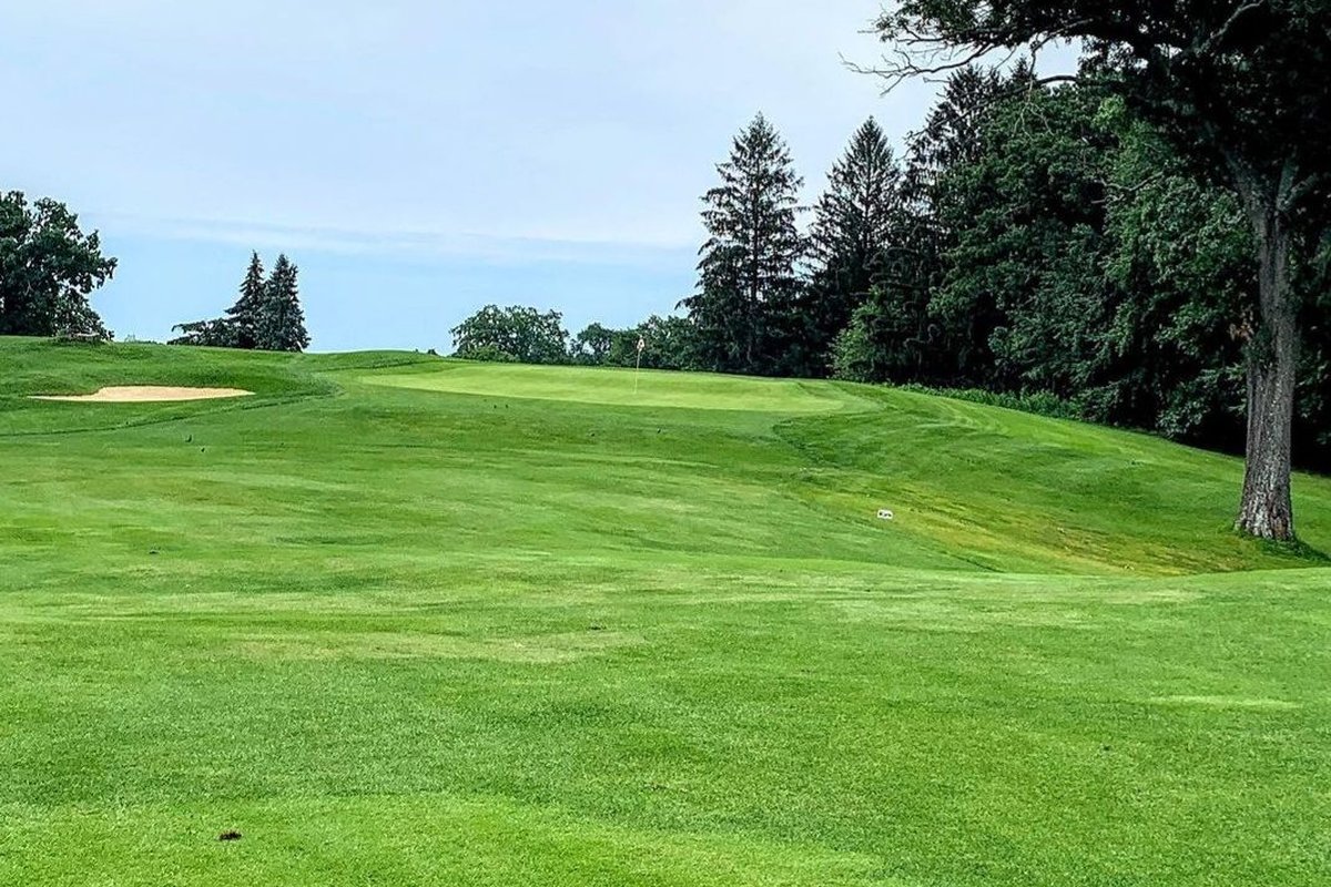 Rolling fairway at D W Field Municipal GC in Brockton, MA with a visible sand bunker, lush green grass, and tall trees bordering the hole