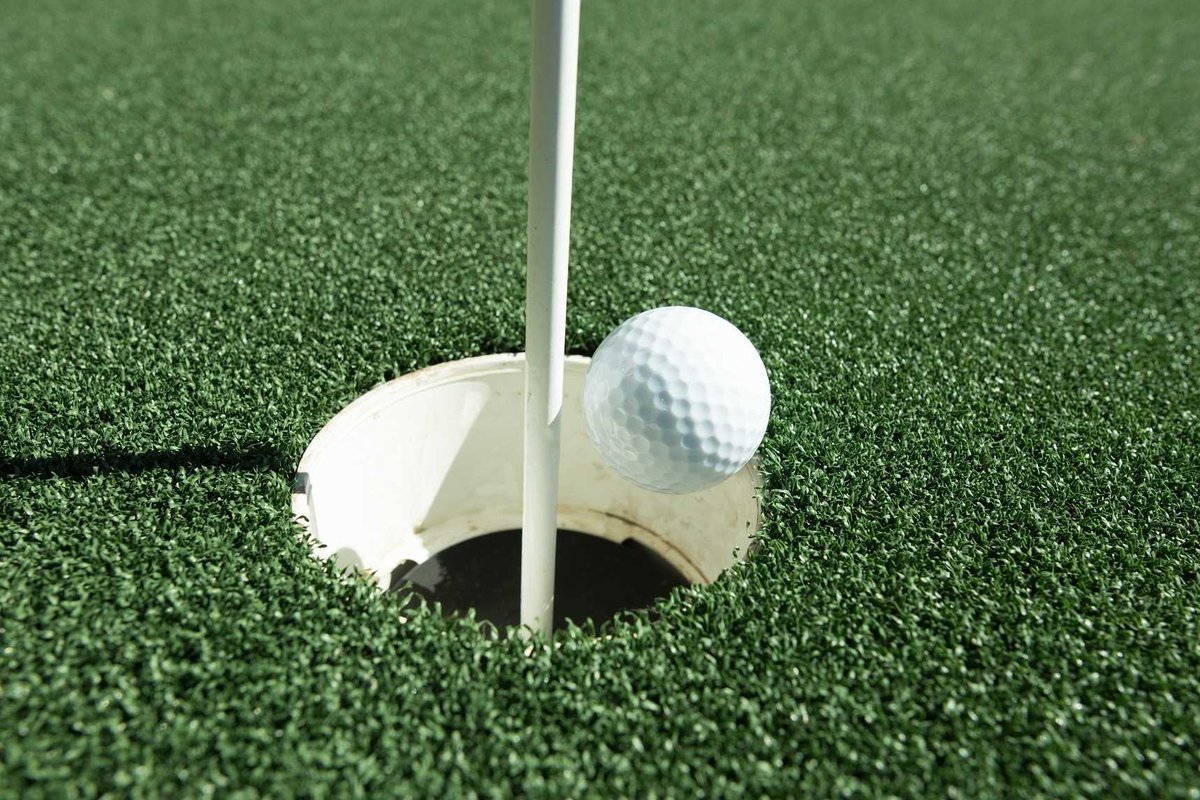 Golf ball rests on the edge of the cup beside the flagstick on a closely mown green at Dennis Highlands GC in Dennis, MA