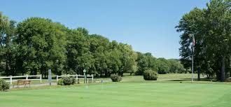 Lush green putting green at Ellinwood Country Club in Athol, MA with trees lining the fairway under a clear blue sky