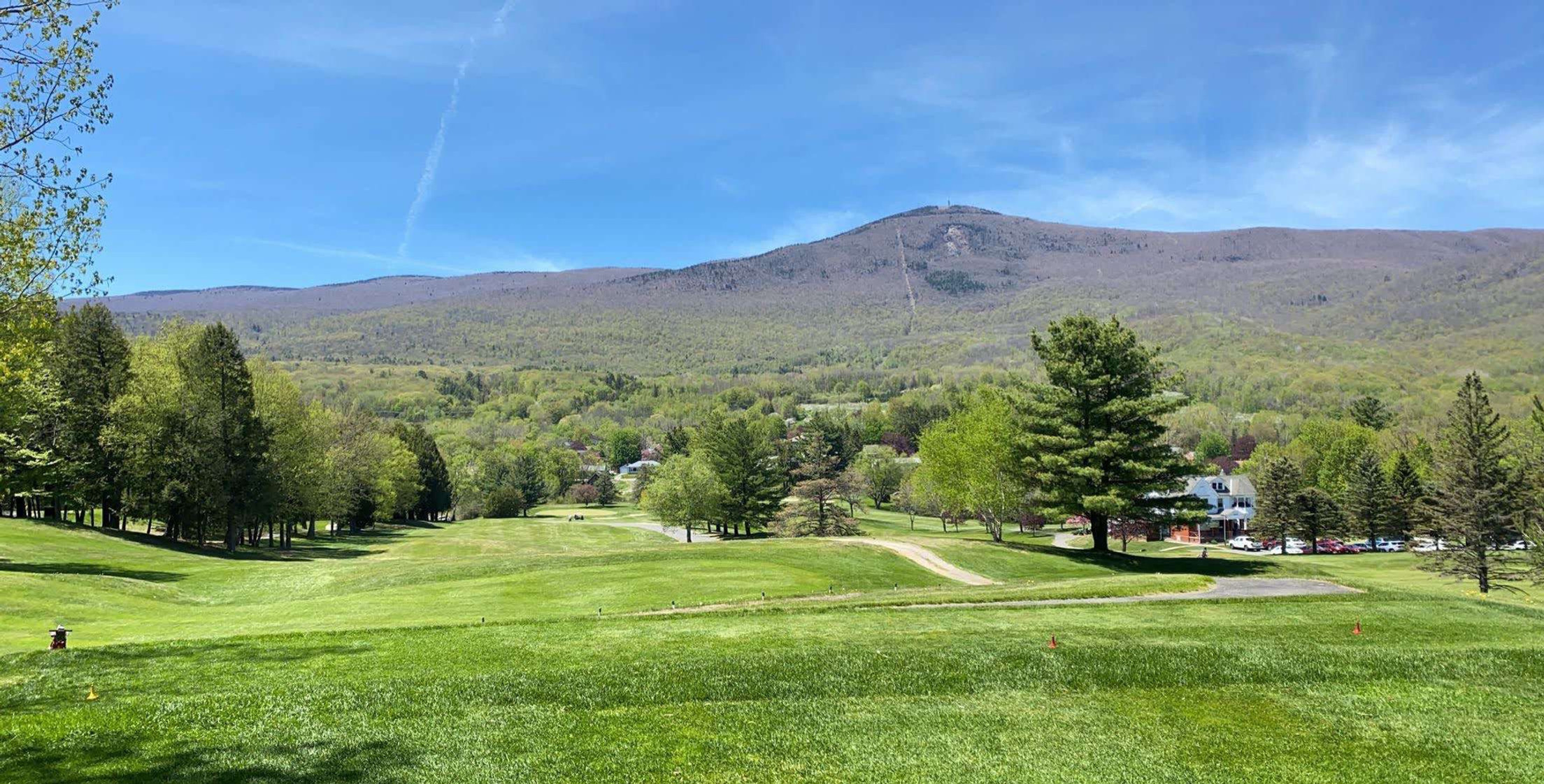 Lush fairway at Forest Park Adams Country Club in Adams, MA with trees, distant houses, and rolling mountains under blue sky