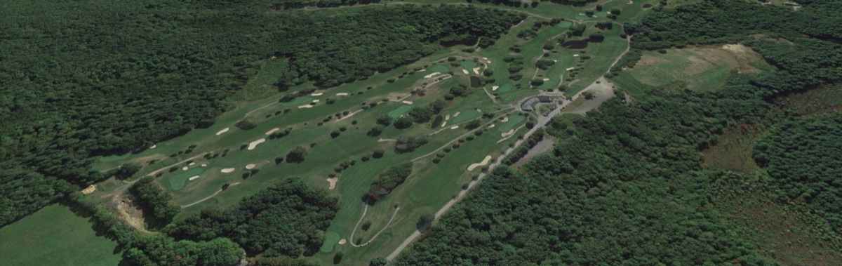 Aerial view of Heritage Country Club golf course in Charlton, MA featuring tree-lined fairways, greens, sand bunkers, and wooded surroundings