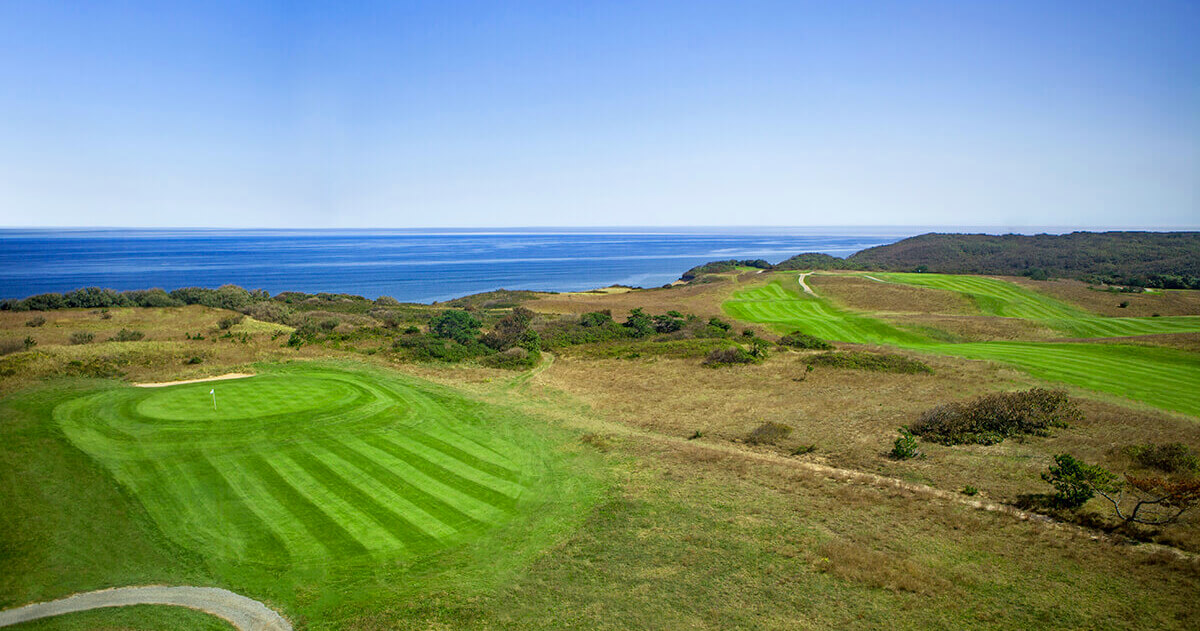 Elevated view of Highland Links Golf Course in Truro, MA with striped fairways, green, rough terrain, and ocean in the background