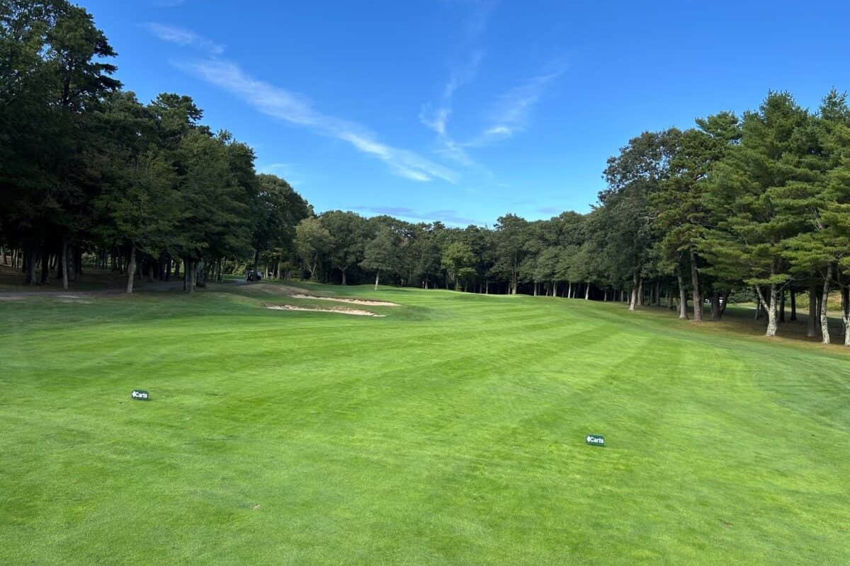Lush fairway at Hyannis Golf Club in Barnstable, MA with sand bunkers on the left, surrounded by dense trees under a clear blue sky