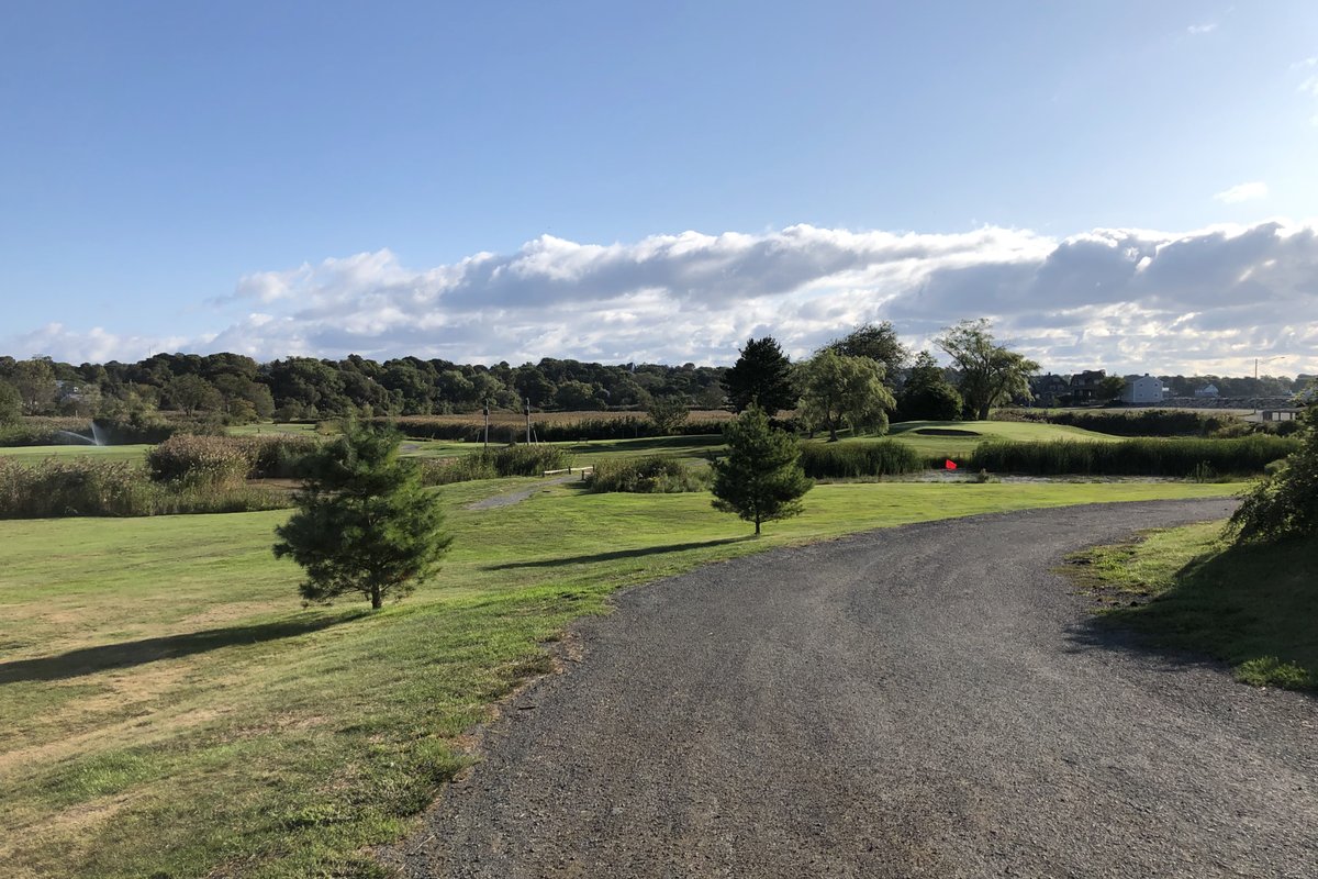 Curved gravel path at Nahant Golf Club at Kelley Greens with manicured fairways, scattered trees, and partly cloudy sky