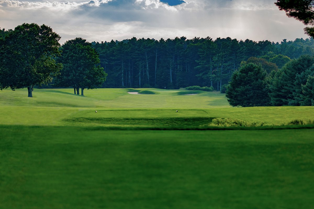 Lush green fairway at North Hill Country Club in Duxbury, MA with sand bunker, trees, and overcast sky in background