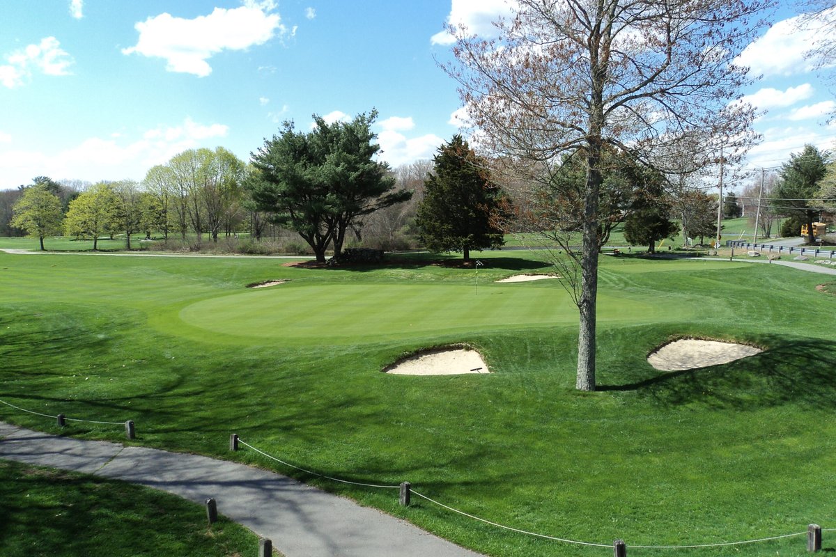 Norton Country Club green surrounded by three white sand bunkers, bordered by trees and vibrant fairways under a blue sky