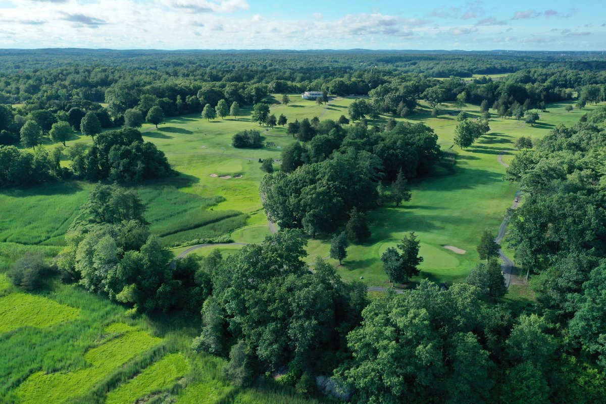 Aerial view of Ould Newbury Golf Club in Newbury, MA with lush fairways, greens, trees, and rolling landscape under blue sky