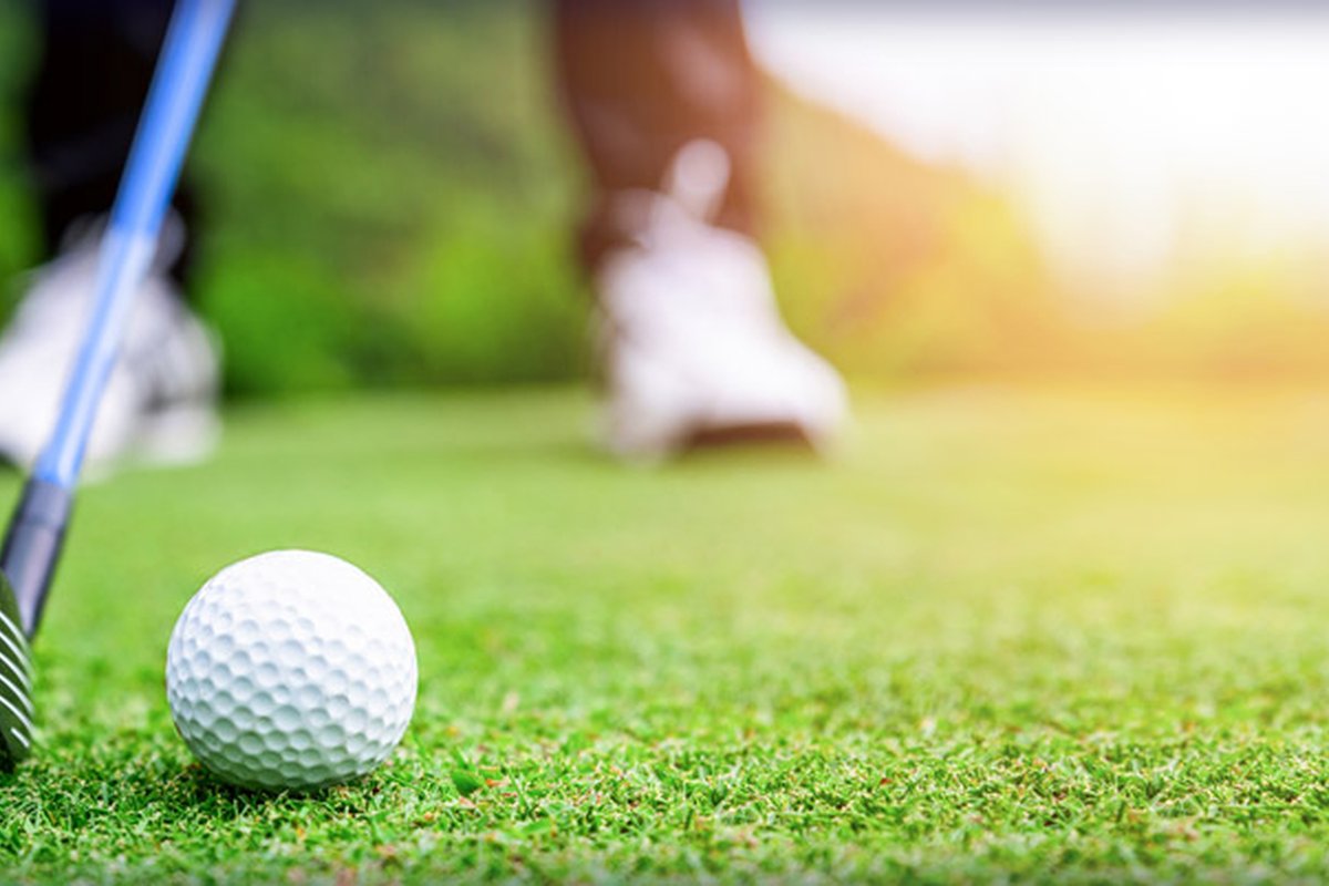 Golf club positioned behind a white golf ball on the green at Country Club of Billerica, golfer in blurred background