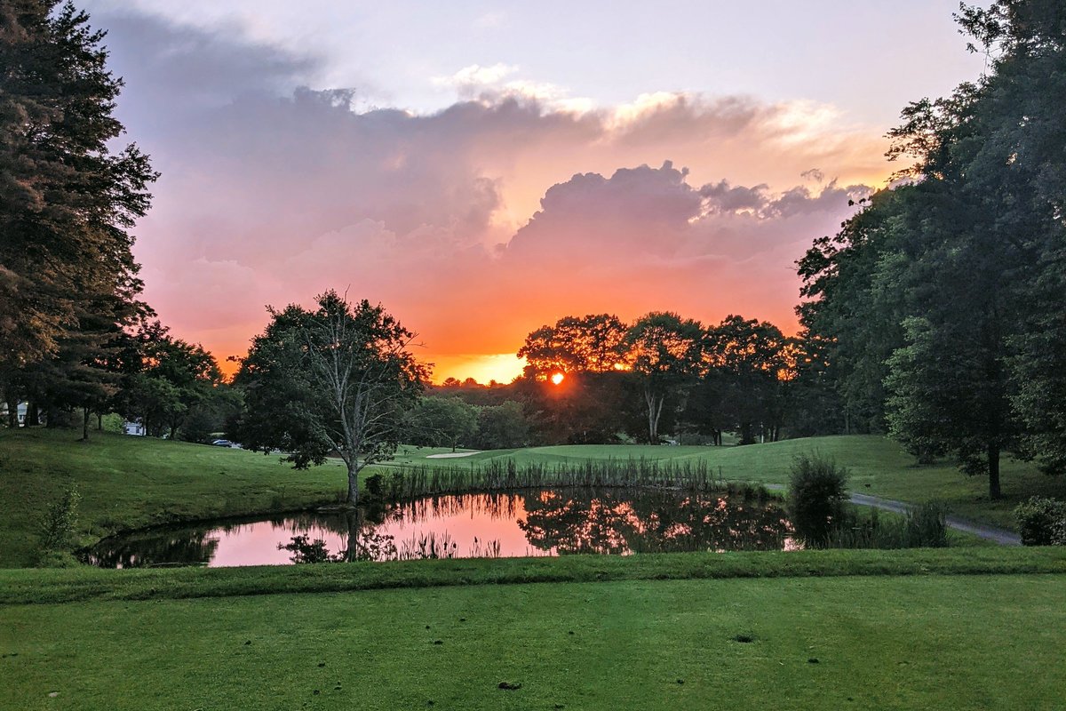 Sunset over a pond at Poquoy Brook Golf Course, Lakeville, MA, with green fairway, trees, and dramatic cloud-filled sky