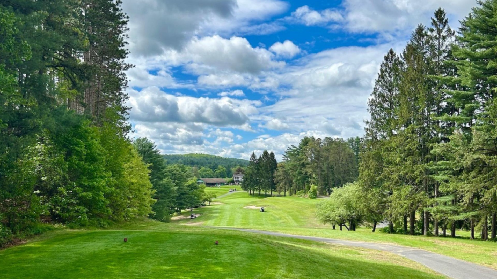 Lush fairway at Quaboag Country Club in Monson, MA with tall trees, rolling hills, and a partly cloudy sky overhead