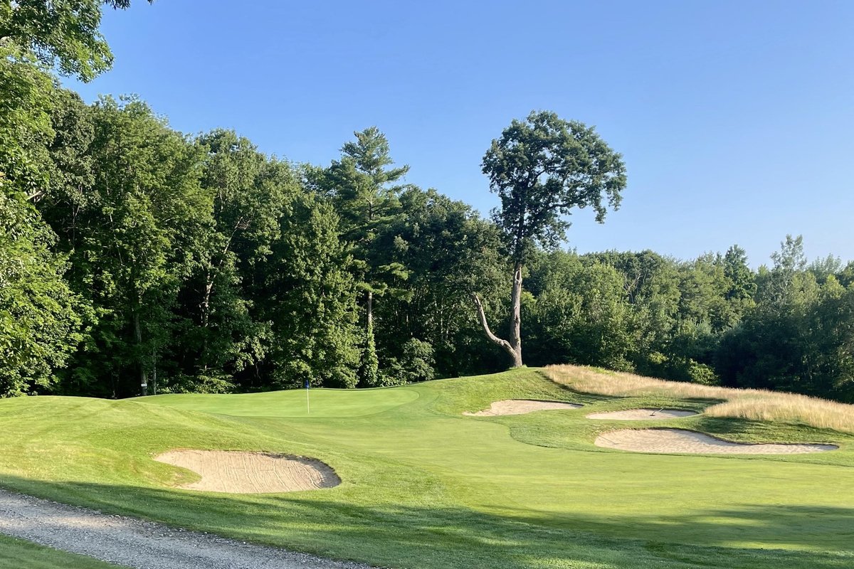 Blissful Meadows Golf Club green bordered by several sand bunkers, lush fairway, trees, and bright blue sky in Uxbridge, MA