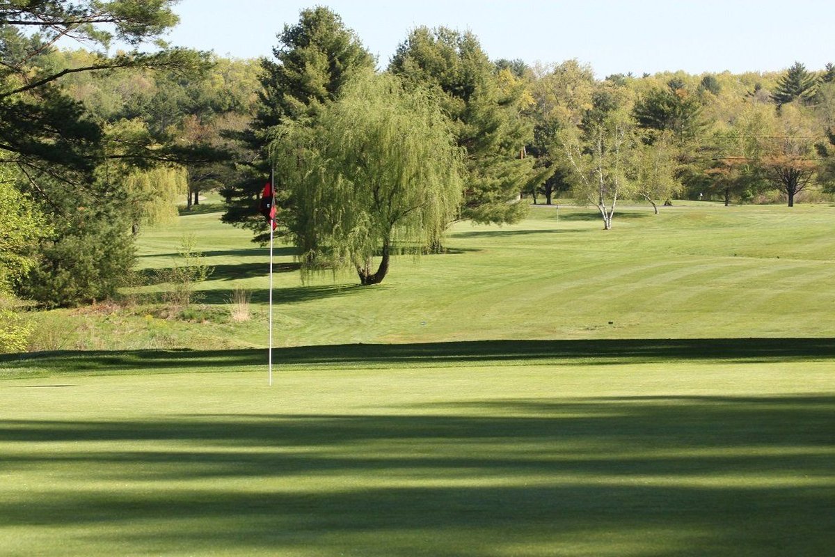 Shaker Farms Country Club green with pin flag, rolling fairway, lush trees, and clear blue sky in Westfield, MA