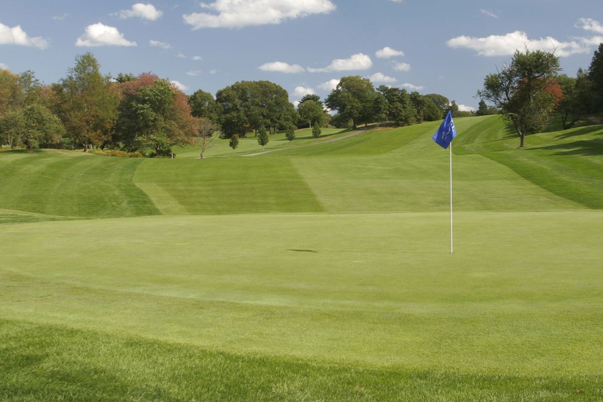Blue flag on green at South Shore Country Club in Hingham, MA with rolling fairways, trees, and partly cloudy sky