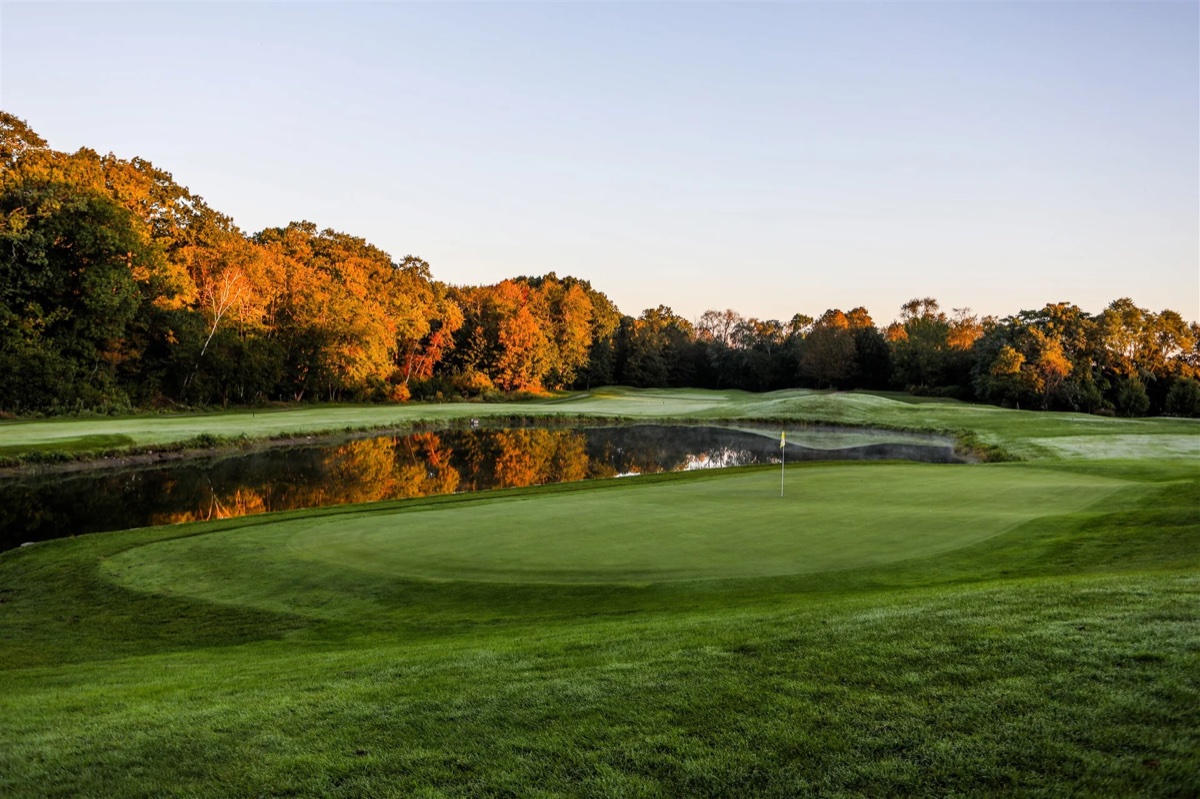 Bradford Country Club green with flagstick, lush fairway, pond reflecting trees, and clear sky at sunset in Haverhill, MA