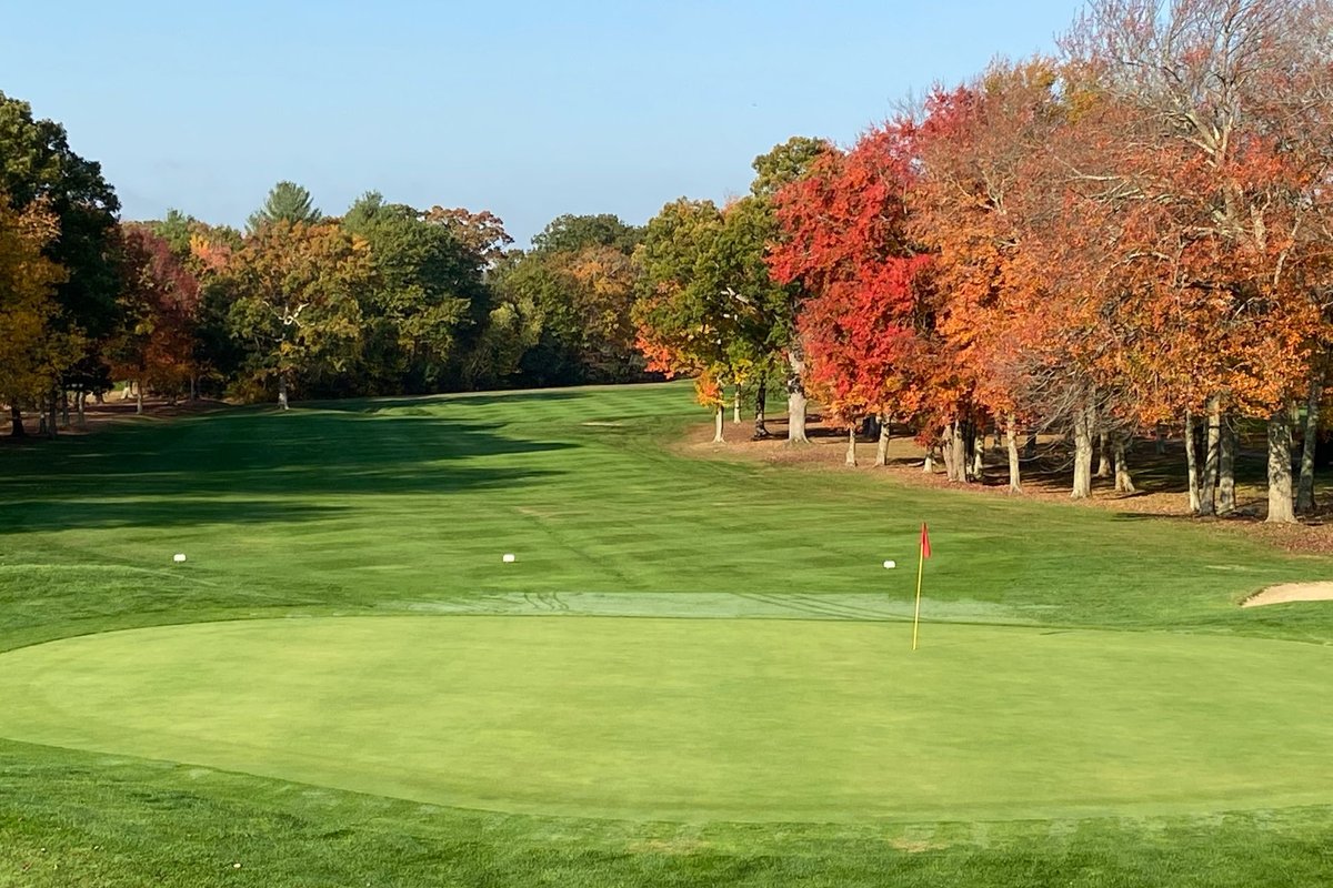 Well-manicured green with red flagstick at Swansea Country Club, bordered by fairway and autumn trees with colorful foliage