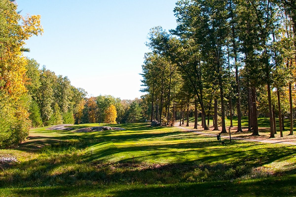 Sunlit fairway at Swanson Meadows GC in Billerica, MA lined with tall trees, lush grass and autumn foliage under blue sky