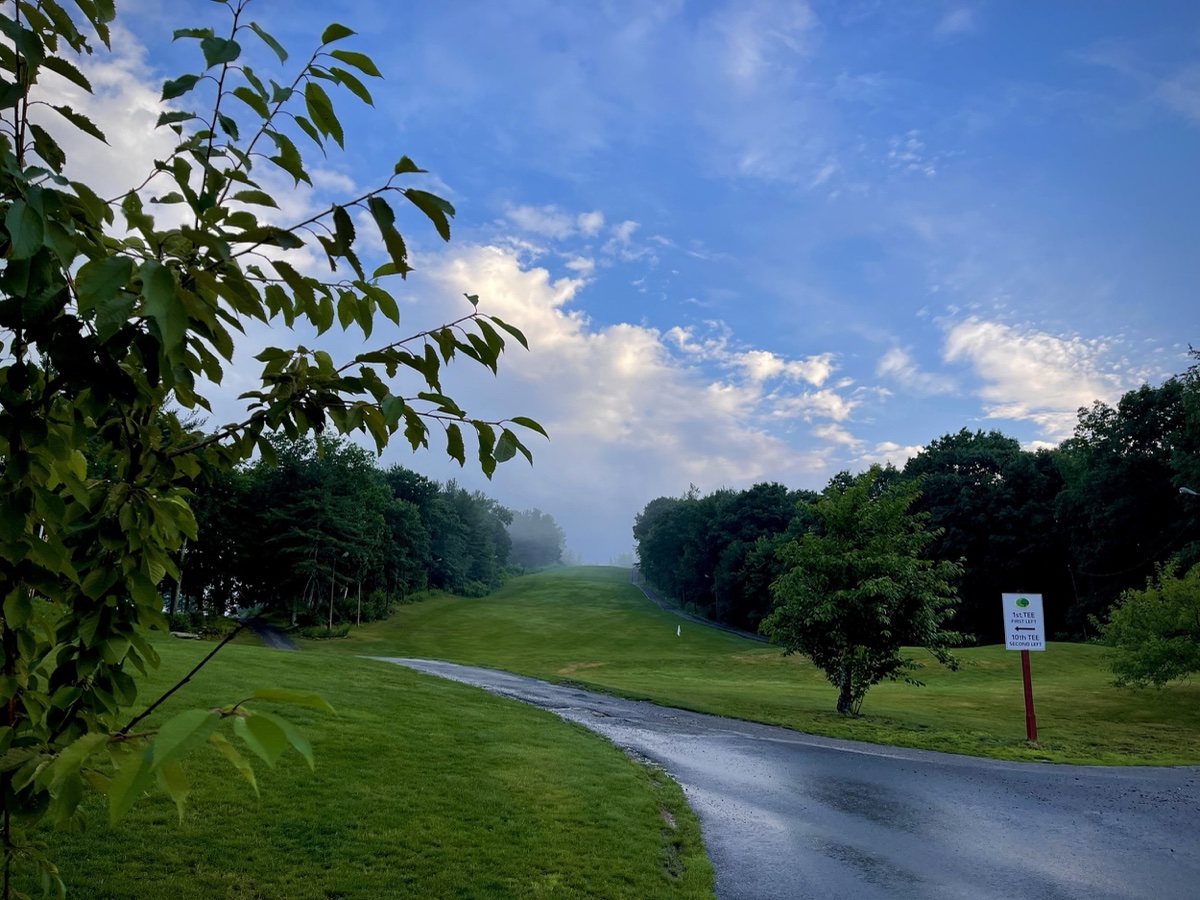 Curving paved cart path at The Woods of Westminster with lush fairway, trees lining both sides, and blue sky with clouds