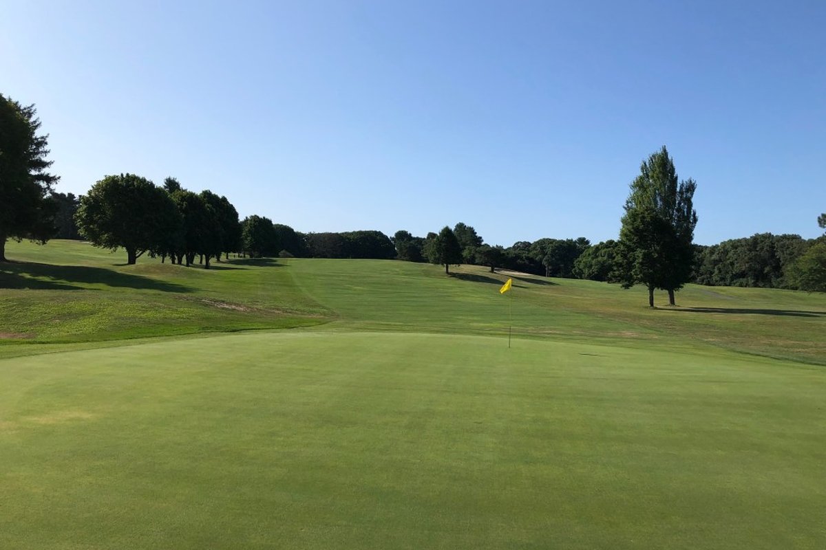 Sunny view across the green toward fairway at Unicorn Golf Course, Stoneham, MA with trees lining gently sloping hills