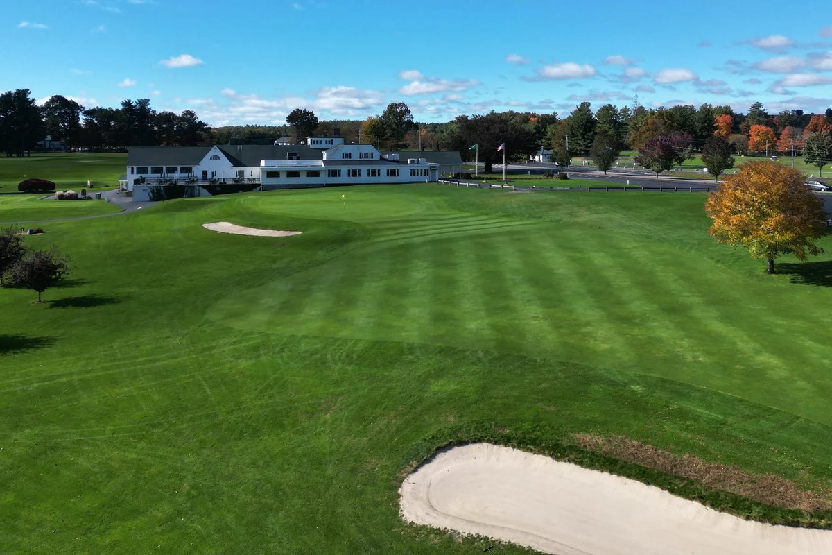 Clubhouse at Wachusett Country Club with green fairway, two sand bunkers, autumn trees, and a clear blue sky