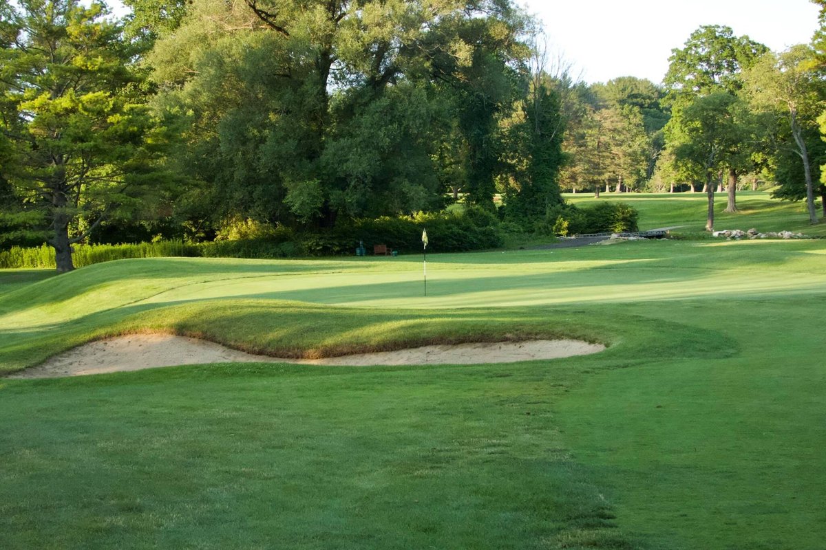 Green at Wahconah Country Club in Dalton, MA with a sand bunker in front, surrounded by lush trees and a clear sky