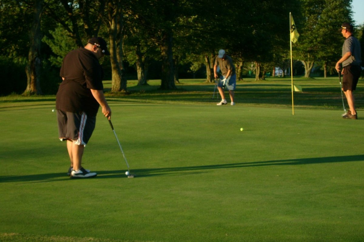 Three golfers putting on a sunny green surrounded by trees at Wampanoag Golf Course in Swansea, MA