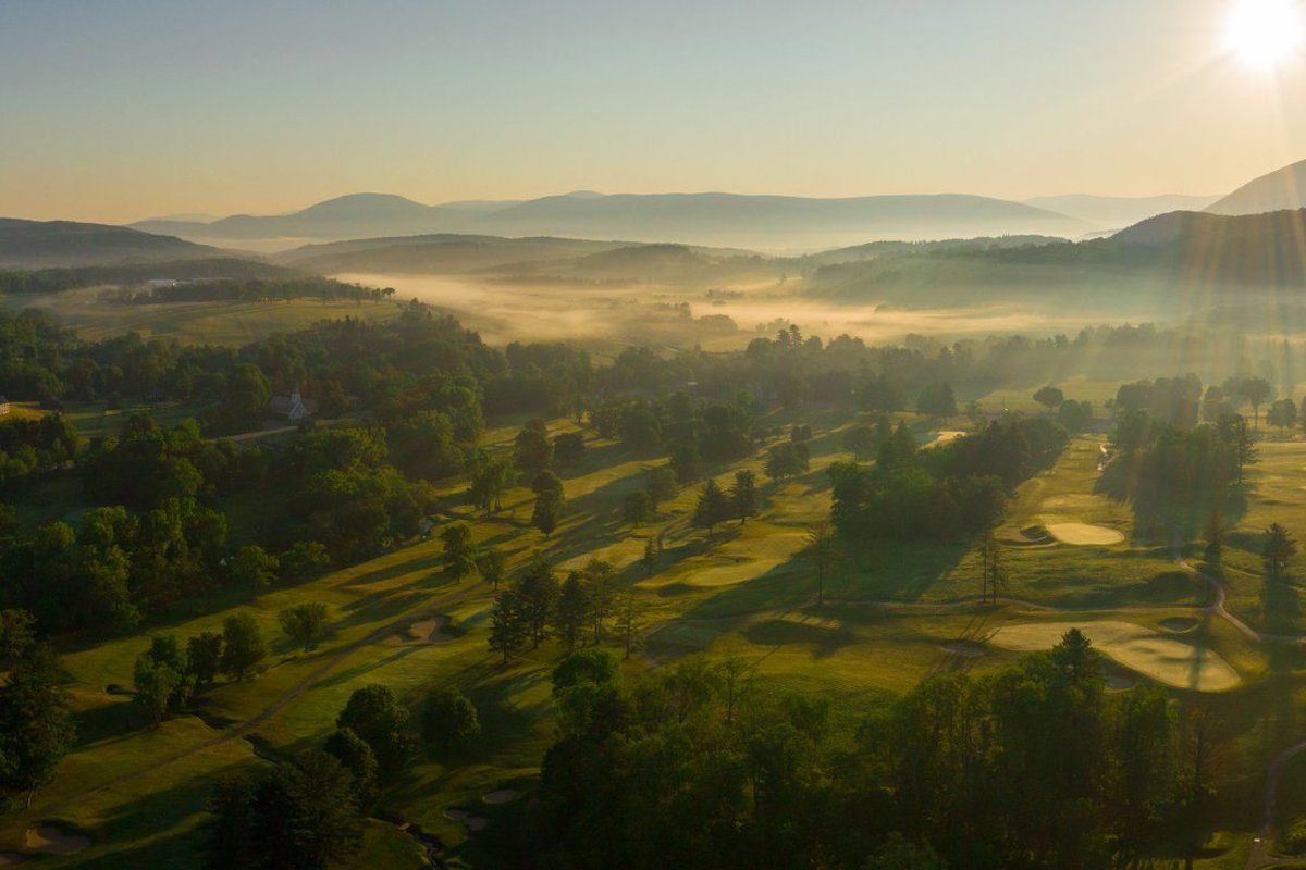Aerial view of Waubeeka Golf Links in Williamstown, MA at sunrise with misty fairways, tree-lined greens, and distant hills.