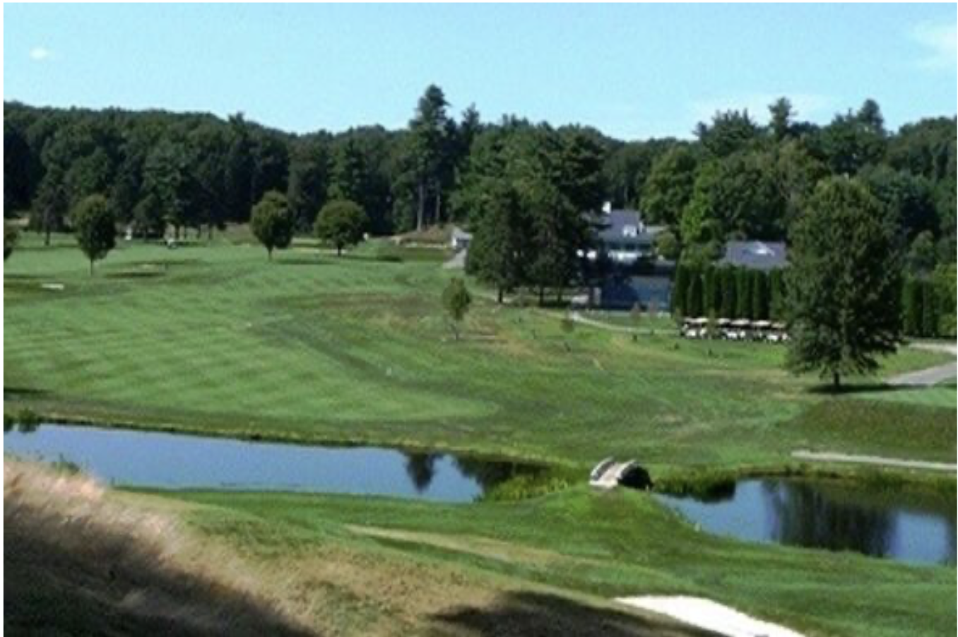Wayland Country Club fairway with striped mowing patterns, bordered by trees, clubhouse in the background, pond and sand bunker in foreground