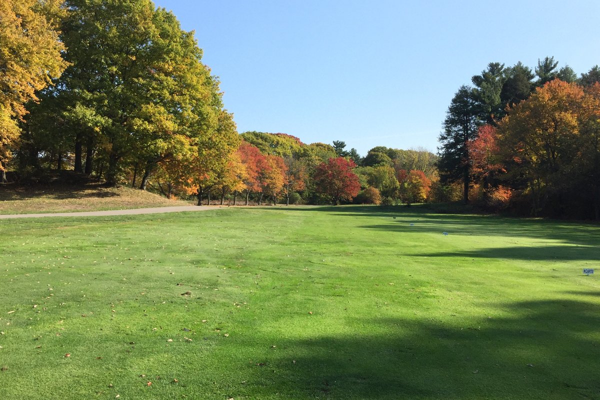 Lush green fairway at Robert T Lynch Municipal GC in Brookline, MA bordered by colorful autumn trees under clear blue sky
