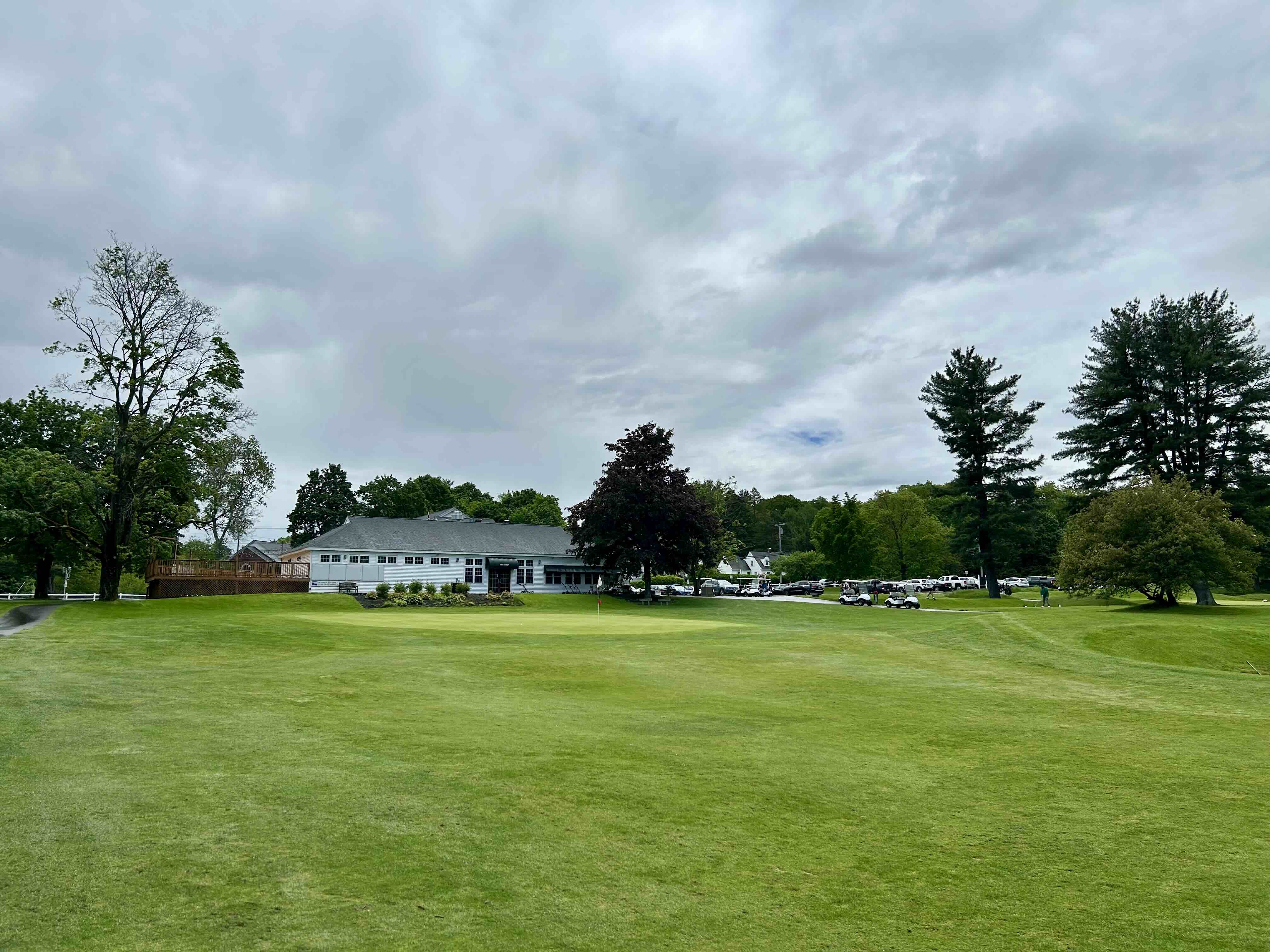 Clubhouse at Westboro Country Club with lush green fairway, scattered trees, parked golf carts, and cloudy sky above