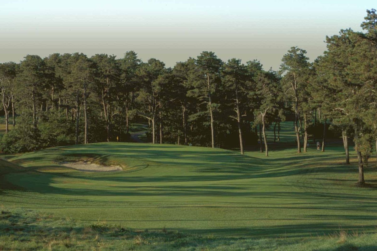 Wide fairway at Captains Golf Course Starboard in Brewster, MA lined with tall pine trees and a sand bunker on the left
