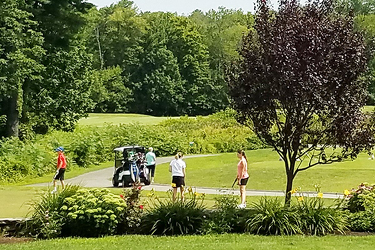 Golfers prepare to tee off on a lush par 3 hole at Cyprian Keyes GC, with a golf cart, trees, and gardens in view.