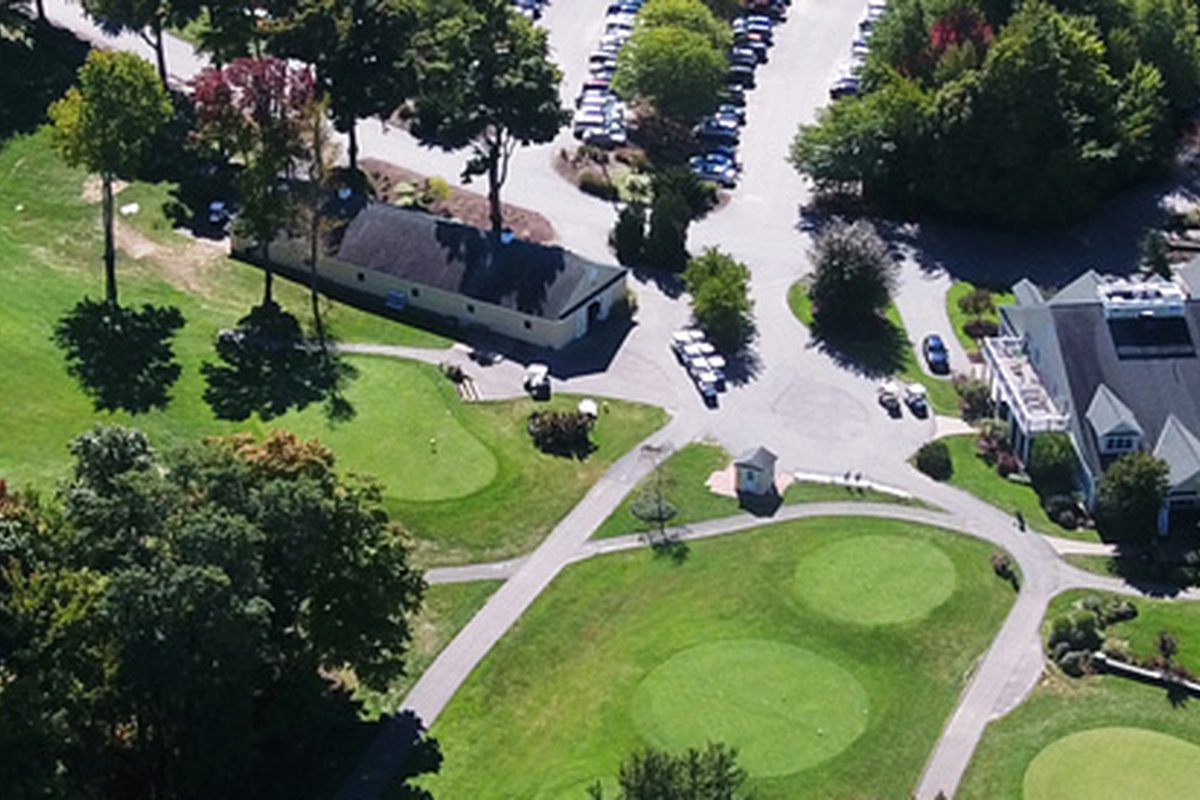 Aerial view of Cyprian Keyes Golf Club showing practice putting greens, tree-lined paths, clubhouse, and nearby parking lot in Boylston, MA