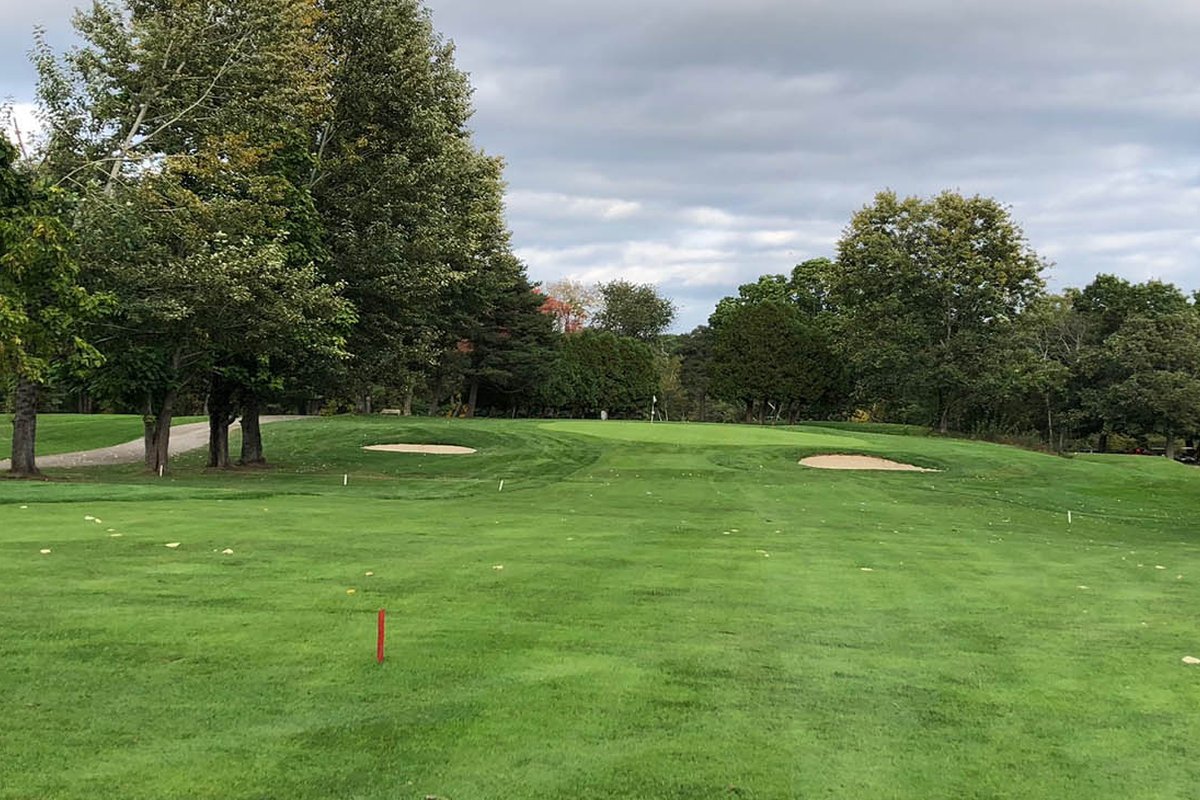 Wide fairway at Chelmsford Country Club with two sand bunkers guarding a green, surrounded by tall trees under a cloudy sky