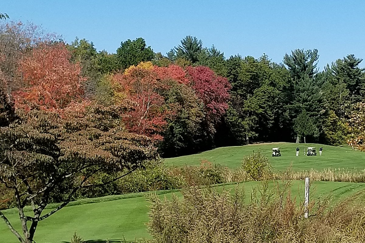 Chicopee Country Club fairway with two golf carts, lush green grass, autumn trees with vibrant foliage, clear blue sky