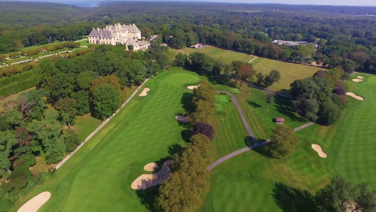 Aerial view of Cold Spring Country Club fairways and bunkers surrounded by trees with a large estate building in the background